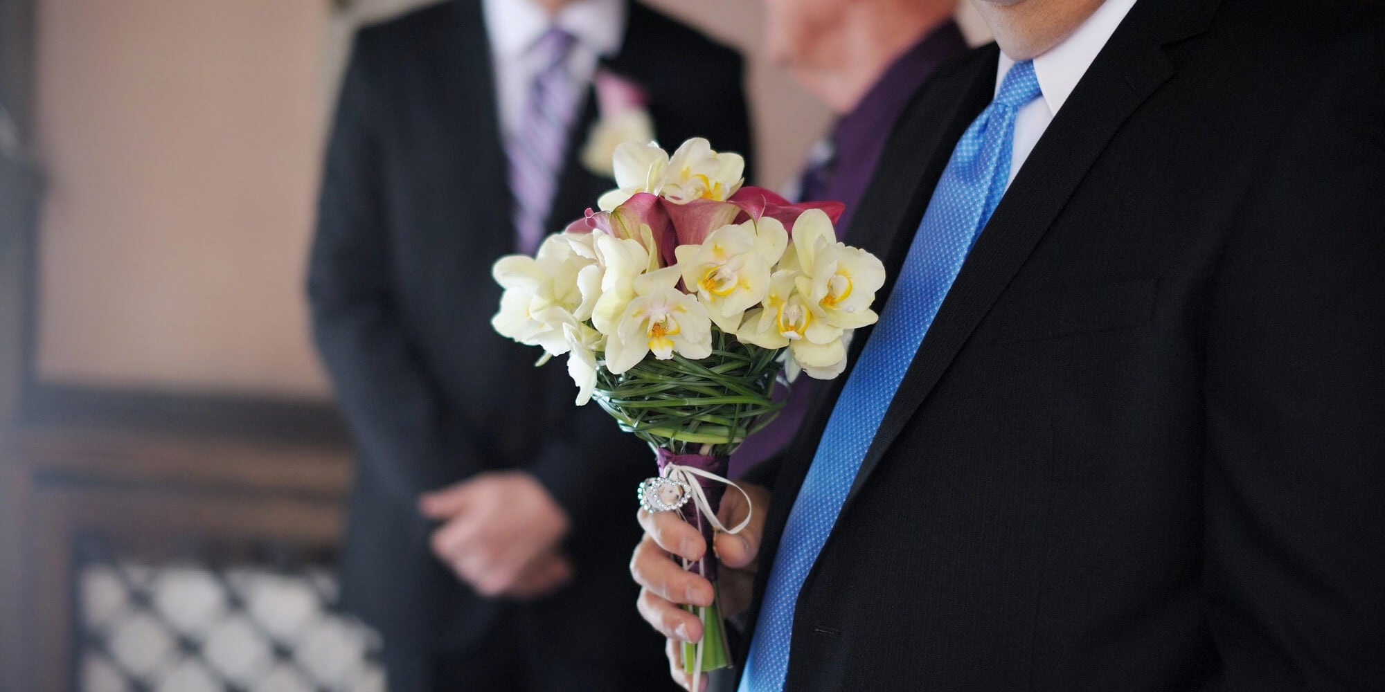 father in his suit holding a bouquet of flowers at wedding ceremony