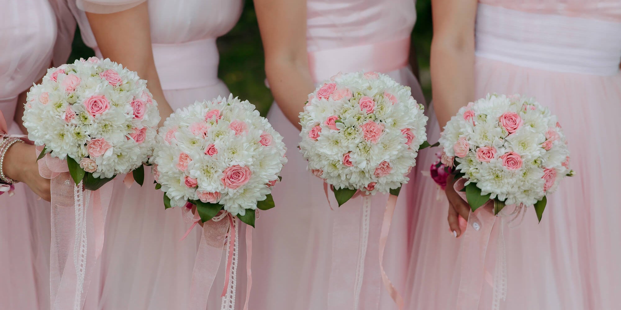 A group of women standing in pink dresses that are holding bouquets of pink and white flowers