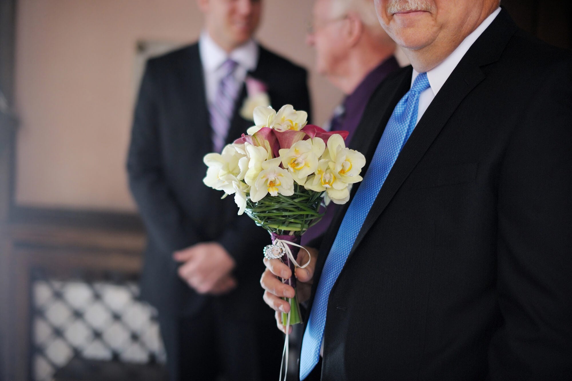 father in his suit holding a bouquet of flowers at wedding ceremony