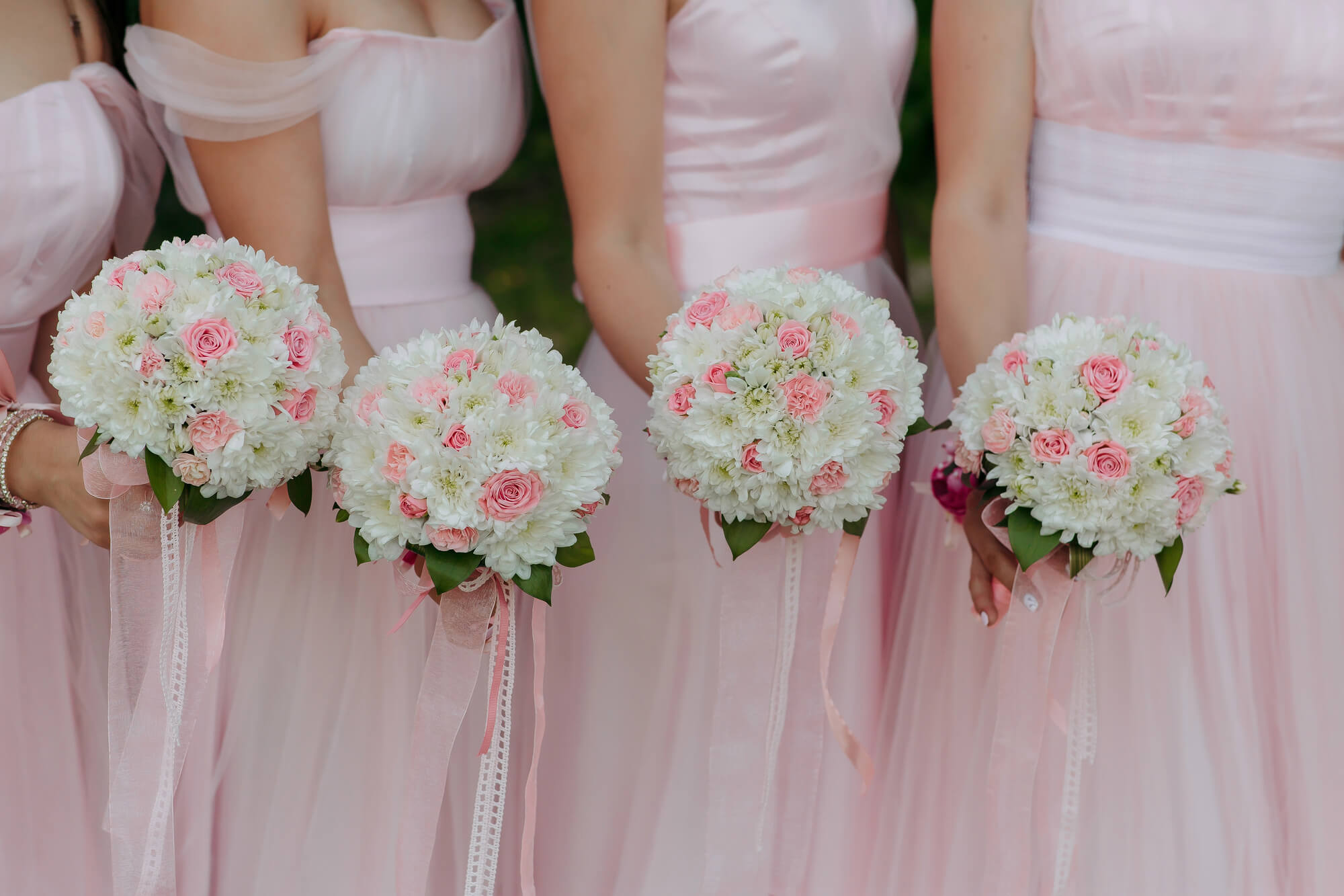 A group of women standing in pink dresses that are holding bouquets of pink and white flowers