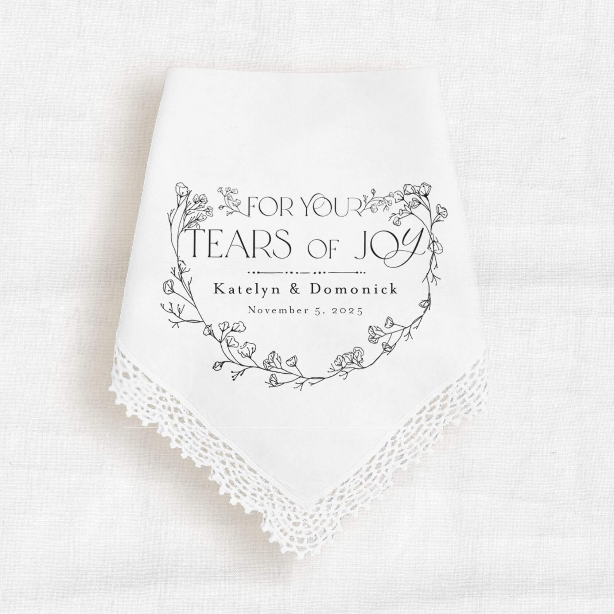 lace handkerchief with a message that reads for your tears of joy.  Personalized with the bride name, groom name and wedding event date.  The text is above a black stenciled graphic of leaves